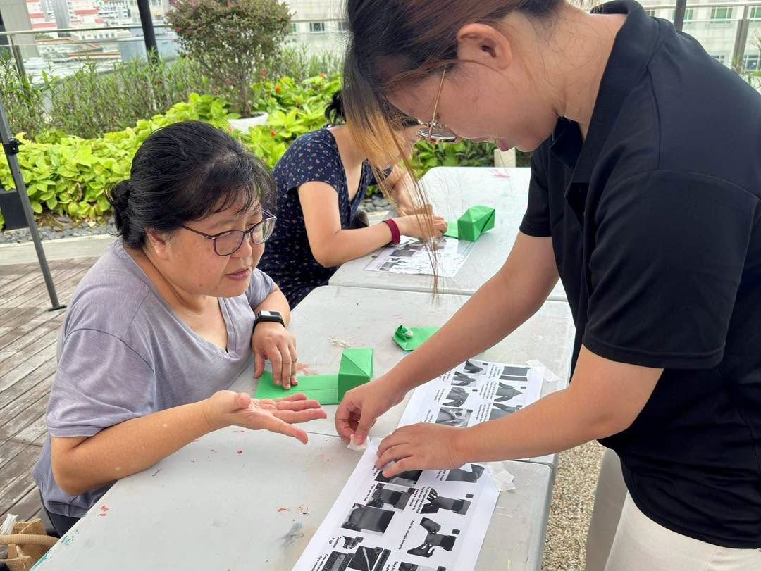 Three participants engaged in paper folding workshop outdoors