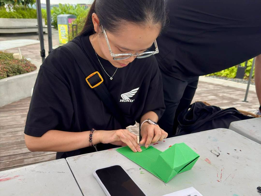 Participant folding green origami paper craft at outdoor seating area