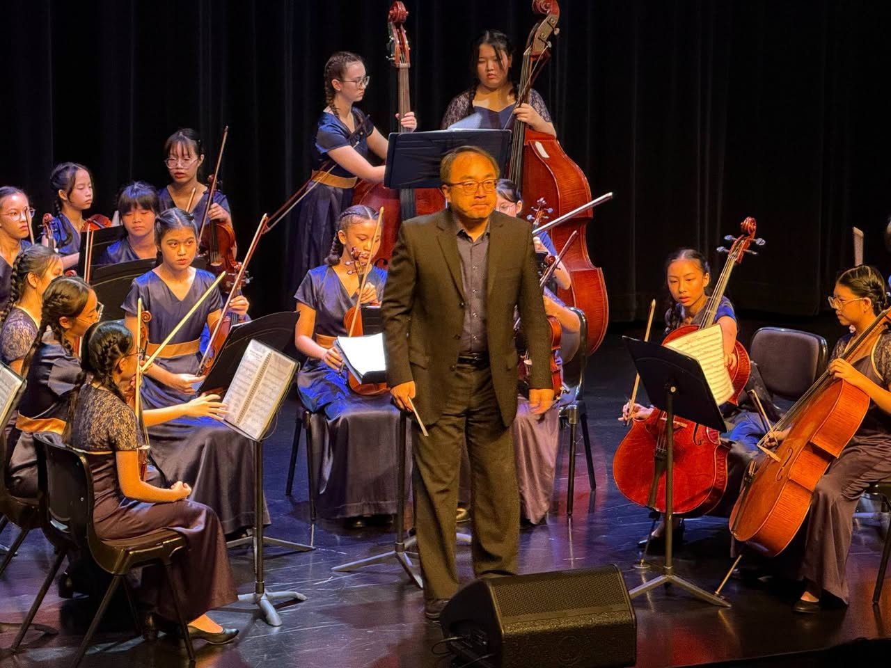 Conductor leading musicians on stage under theatrical lighting
