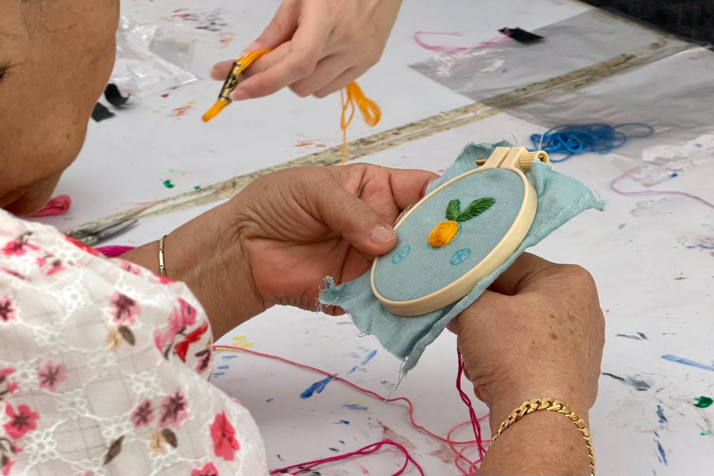 Close-up of hands embroidering a pineapple motif on light blue fabric in a wooden hoop